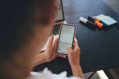 Çalışma saatleri içinde bilgisayarla masada otururken cep telefonu ve mesajlaşma kullanan yüksek açılı ekinsiz serbest çalışan