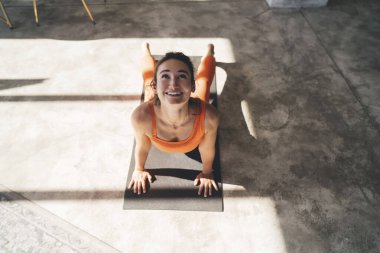 Spor kıyafetleriyle gülümseyen güzel bir bayandan Bakışlarla Yukarı Yüzlü Köpek pozu alıp gün ışığında yoga yaparken.