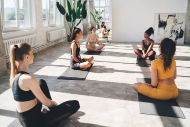 Nilüfer çiçekli mindere oturmuş, yoga yaparken, meditasyon yaparken ve spor salonunda boş vakitlerin tadını çıkarırken birbiriyle konuşan çok kültürlü genç kadınlar.