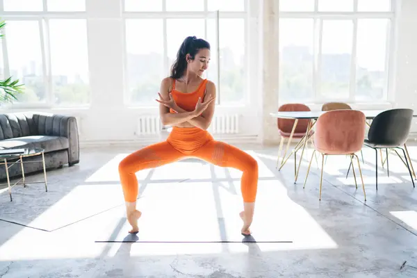 stock image Full body of young lady in sportswear standing in Goddess pose or Utkata Konasana while practicing yoga exercise in modern studio