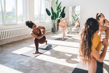 Genç, çok kültürlü bayan arkadaşların gülümseyip, Hilal hareketlerini çalışırken bacaklarının esnemesi ve spor salonunda bakışlarının açılması.