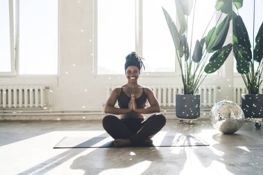 Anjali Mudra 'da mindere oturmuş spor kıyafetli Afro-Amerikan atletik kadın vücudu ya da namaste elleriyle yoga yapan fok balığı pozisyonu.