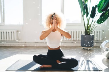 Yoga yaparken mindere oturup meditasyon yapan kıvırcık saçlı genç bir kadın vücudu ya da baş aşağı ve namaste ellerle fok balığı pozisyonu.