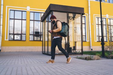 Şehir caddesinde cep telefonuyla sohbet ederken ceketli, siyah sırt çantalı ve güneş gözlüklü sakallı hippinin vücut tarafı.