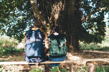 Sırt çantalarıyla, ormandaki büyük ağacın gölgesinde sırtüstü uzanan ve yaz aylarında uzun yürüyüşlere ara veren isimsiz erkek ve dişinin arka plan görüntüsü.