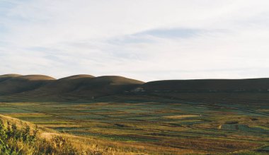 Vadinin resimli manzarası. Tarım tarlaları ıslak tarlalarla kaplıydı ve kırsal kesimlerde kuru çim tepeleriyle çevriliydi. Gün batımında bulutlu mavi gökyüzünün altında yerleşim yolları vardı.