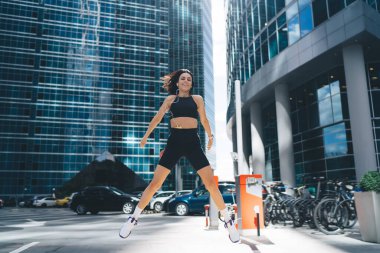Siyahi spor giyim ve spor ayakkabılarıyla heyecanlı kadın sporcular modern şehir merkezindeki caddenin üzerinde zıplıyorlar.