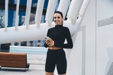 Çağdaş binanın yanında durup cep telefonuyla sohbet ederken gülümseyen ve kameraya bakan siyah elbiseli neşeli genç bayan.