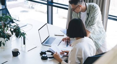 Akıllı günlük kıyafetlerle, ofiste dizüstü bilgisayarla ve dizüstü bilgisayarlı bir fincan kahveyle, proje üzerinde çalışırken etkileşim içinde olan iş arkadaşları.