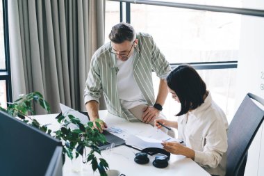 Modern çalışma ortamında dokümanlar ve dizüstü bilgisayarlar üzerinde çalışan şık giyimli genç meslektaşların yüksek açısı.