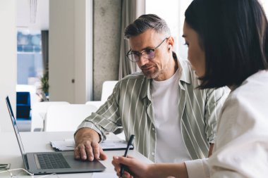Resmi giysiler ve gözlük takan ciddi çeşitli girişimciler bilgisayar başında oturmuş parlak ofis odasındaki proje üzerinde çalışırken notlar alıyorlar.