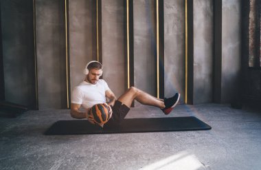 Spor kıyafetleri ve kulaklıklarla spor salonunda antrenman yaparken karın kasları ve ağır toplarla antrenman yapan konsantre bir erkek sporcu vücudu.