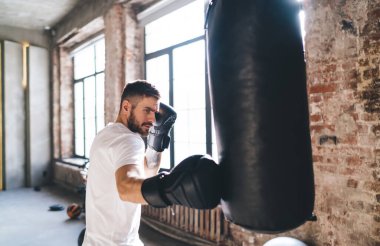 Beden eğitimi sırasında boks eldivenli, kum torbasını yumruklamak ve birbiri ardına saldırmak isteyen erkek sporcuların yan görüntüsü.