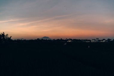 Turuncu gökyüzünün dağdaki ve kırsal alandaki manzarası yaz mevsiminde palmiye ağaçları ve turistlere göz zevki veren beyaz binalar.