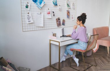 Genç milenyum kadın bilgisayar cihazıyla evde oturup uzaktan kumandayla çalışıyor. Webinar kursuyla çevrimiçi öğrenen kız öğrenci uzaktan çalışmak için taşınabilir netbook kullanıyor