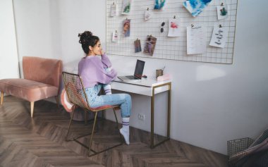 Genç milenyum kadın bilgisayar cihazıyla evde oturup uzaktan kumandayla çalışıyor. Webinar kursuyla çevrimiçi öğrenen kız öğrenci uzaktan çalışmak için taşınabilir netbook kullanıyor