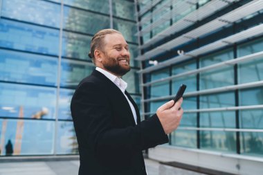 Şen şakrak işadamının, modern cam ofis binasının yanında dikilirken yan bakışları gündüz gözüyle caddenin yansıması ve cep telefonuyla mesajlaşması.