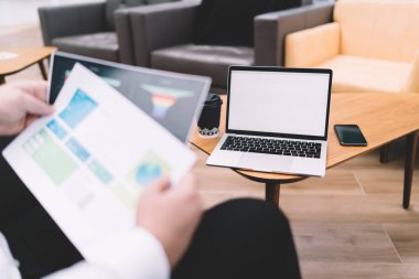 Anonim bir erkek çalışanın ahşap masada dizüstü bilgisayarlı akıllı telefon ve bir fincan kahveyle modern çalışma alanındaki çizelgeler üzerinde çalışması.