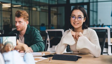 Optik gözlüklü mutlu kadın çalışanın portresi birlikte çalışma alanındaki başlangıç projesini geliştirirken kameraya gülümsüyor, modern dokunmatik pedi olan neşeli kadın işbirliği için poz veriyor.