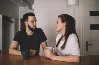 Romantik bir buluşma sırasında mutfakta kahve içerken birbirlerine aşkla bakan ciddi bir genç adam ve kadın.