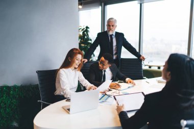 Çağdaş konferans odasında iş stratejisi üzerinde çalışırken resmi kıyafetli bir grup çok ırklı iş arkadaşı masada oturuyor.