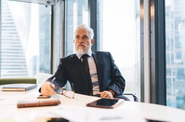 Zarif takım elbiseli ve kravatlı dalgın işadamı modern ofisin penceresine karşı başlangıç projesi üzerinde çalışırken masada oturuyor.