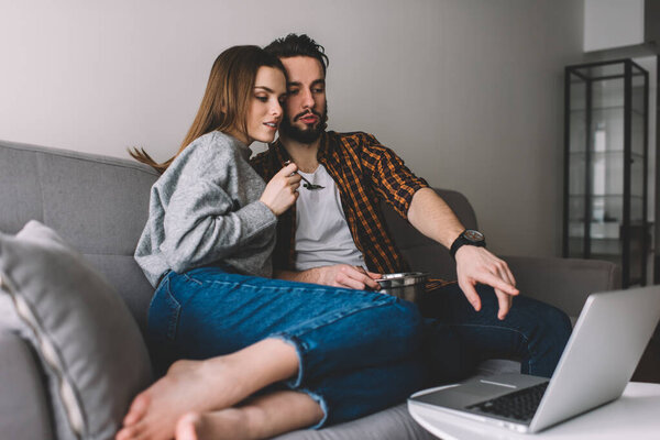 Caucasian couple in love watching interesting movie browsed on modern laptop computer connected to home WIFI in living room, good looking male and female reading publication in social media