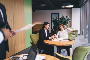 Modern ofiste kağıt akıllı telefonlar ve dizüstü bilgisayarlar ile oturup yuvarlak masalarda dururken resmi giysiler içinde proje tartışan bir grup iş arkadaşı.