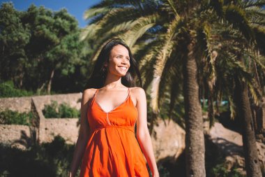 Kırmızı elbiseli, gülümseyen ve hayal kuran genç bir bayandan, palmiye ağaçlarına karşı yaz tatilinin keyfini çıkarırken