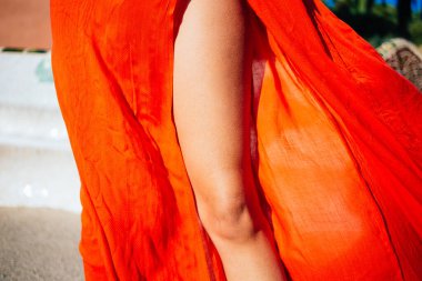 Yaz tatili boyunca kumlu sahilde yeşil ağaçlı parlak turuncu elbiseli isimsiz bir kadın bacağı.