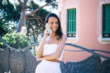 Hafif yaz kıyafetleri içinde etkin bir kadın. Gülümseyen ve cep telefonuyla konuşan yaz tatilinde manzaraya hayran olan ve rahatlatan.