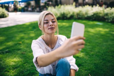 Kafkas kadın vlogger sosyal ağlarda paylaşmak için video içeriği oluşturmak için parkta gün harcıyor, akıllı telefon aygıtındaki selfie fotoğraflarına tıklayarak milenyum hipster kızı poz veriyor