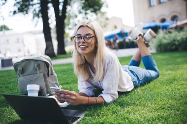 Kameraya gülümseyen, cep telefonu cihazı ve dizüstü bilgisayarı olan neşeli, beyaz bir kadının görsel koruma için optik gözlüklü mutlu kadın portresi.