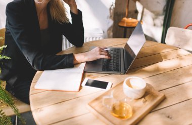 Kafedeki serbest iş sırasında içerik yayınını düzenlemek için dizüstü bilgisayar uygulaması kullanan, siyah ceketli tanınmayan bir kadın internet sitesinde internet bilgilerine göz atıyor.