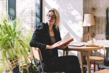 Kişisel planlayıcısı olan düşünceli bir kadın girişimci, organize haftanın programını düşünüyor, optik gözlüklü beyaz kadın hakkında kafa yoruyor ve düşünceli bakışlarını başka yöne çeviriyor.