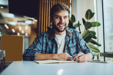 Sakallı, güler yüzlü, şık bir erkek öğrenciden ev ödevlerini yaparken uzaktan öğrenip test için hazırlanan bir not defteri.