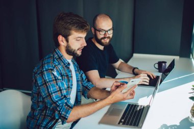 Ofiste masa başında çalışırken akıllı iş adamına akıllı telefon ekranını gösteren akıllı gündelik bilgisayarlı odaklanmış iş adamı