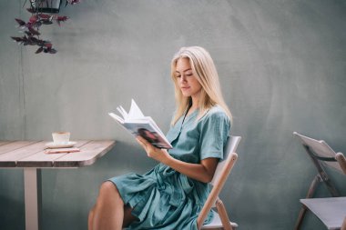 Sokak kafeteryasında eğlenirken edebiyat kitabı okuyan çekici beyaz kadın, entellektüel eğitim, entellektüel eğitim ve entellektüel eğitim ile en çok satan kitaplardan zevk almak için hafta sonunu harcayan genç kadın.