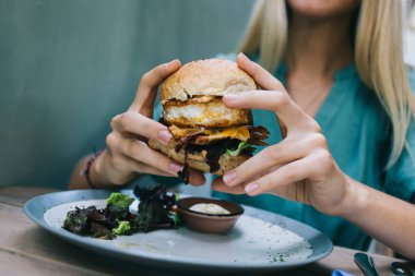 Kırbaçlanmış kadın lezzetli sokak yemekleri yediği için hile yapıyor. Karışık malzemeli burger, Amerikan kalorili akşam yemeği sırasında apetito ile susamlı çizburger yiyen kadın.
