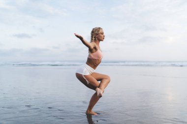 Beyaz, zayıf bir kadın vücudunu pozitif ve sağlıklı tutuyor. Haftasonunu yoga pratiği için deniz kenarında geçiriyor. Sakin, formda bir kız bütünsel iyileşme için spor hatha egzersizi yapıyor.