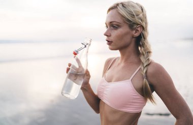 Aktif kıyafetli güzel bir kadın elinde su şişesi tutan eğitim egzersizini düşünüyor. Düşünceli 20 'li yaşlarda genç bir kadın yaz aylarında pilates egzersizi yaparken spor sonuçlarını düşünüyor.