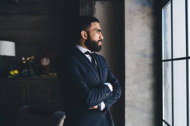 Kaliteli sakallı iş adamının yan görünüşü kollarını modern yatak odasında kavuşturup zor kararlar vermesi.