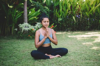 Nilüfer çiçekli poz verip bakışlarını kaçırırken elleri sımsıkı bağlı meditasyon yapan çıplak ayaklı bir kadın vücudu.