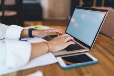 Beyaz tişörtlü isimsiz bir kadın. Akıllı telefon ve dizüstü bilgisayarla ahşap masada oturuyor. Boş ekranlı.