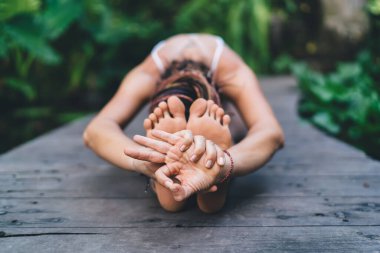 İsimsiz bir kadının parmaklarıyla meditasyon yapması ve tahta köprüde ellerini ve bacaklarını parka uzatarak Paschimottansana yapması.