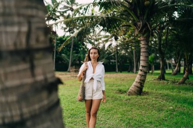 Genç bayanın gülümsemesi ve bakışları yeşil ağacın yanında dururken tropik bir tatil köyünde palmiyeli.