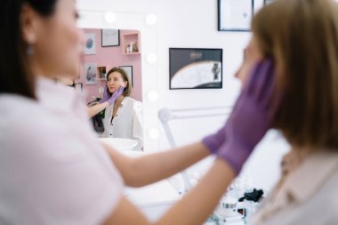 Tedavi sırasında modern kuaförde güzellik prosedürü için cilt hazırlarken müşterinin yüzüne krem sürüyor.