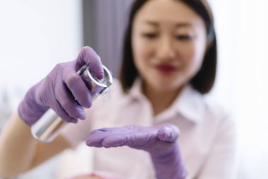 Genç Asyalı kadın güzellik uzmanı koruyucu lateks eldivenler. Klinikte profesyonel tedavi görürken sıvı ürün uyguluyorlar.