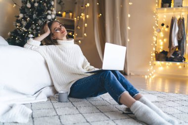 Evde dizüstü bilgisayarla çalışırken rahat, rahat giyinen, gülümseyen ve kameraya bakan genç bir bayan serbest yazar.