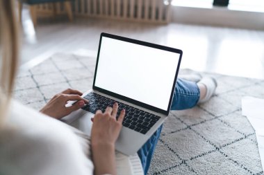 Uzaktan kumanda sırasında netbook kullanarak halı üzerinde oturan ve çevrimiçi pazarda gezinen gündelik kıyafetli meçhul kadın serbest yazardan.